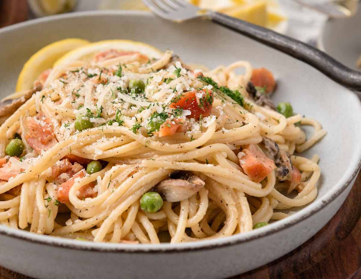 smoked salmon  pasta with peas, mushrooms, and grated parmesan in a low bowl.