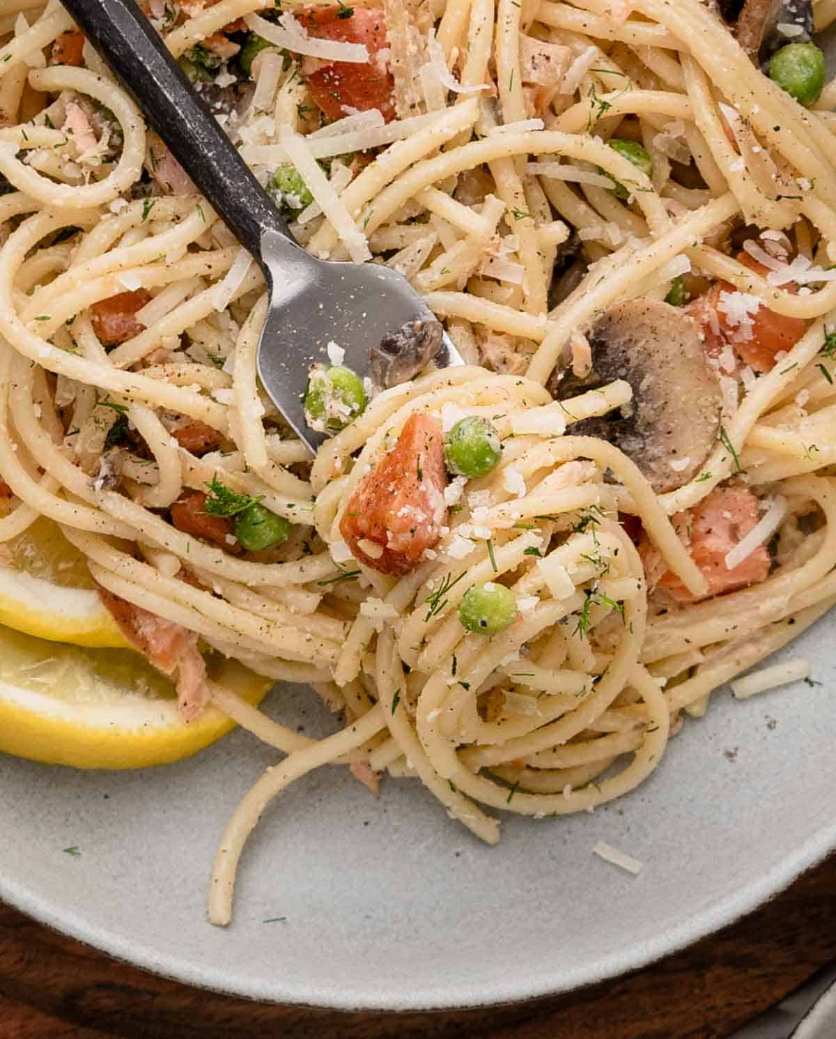 Smoked salmon spaghetti with peas, mushrooms, tomatoes, and herbs twirled on a fork.