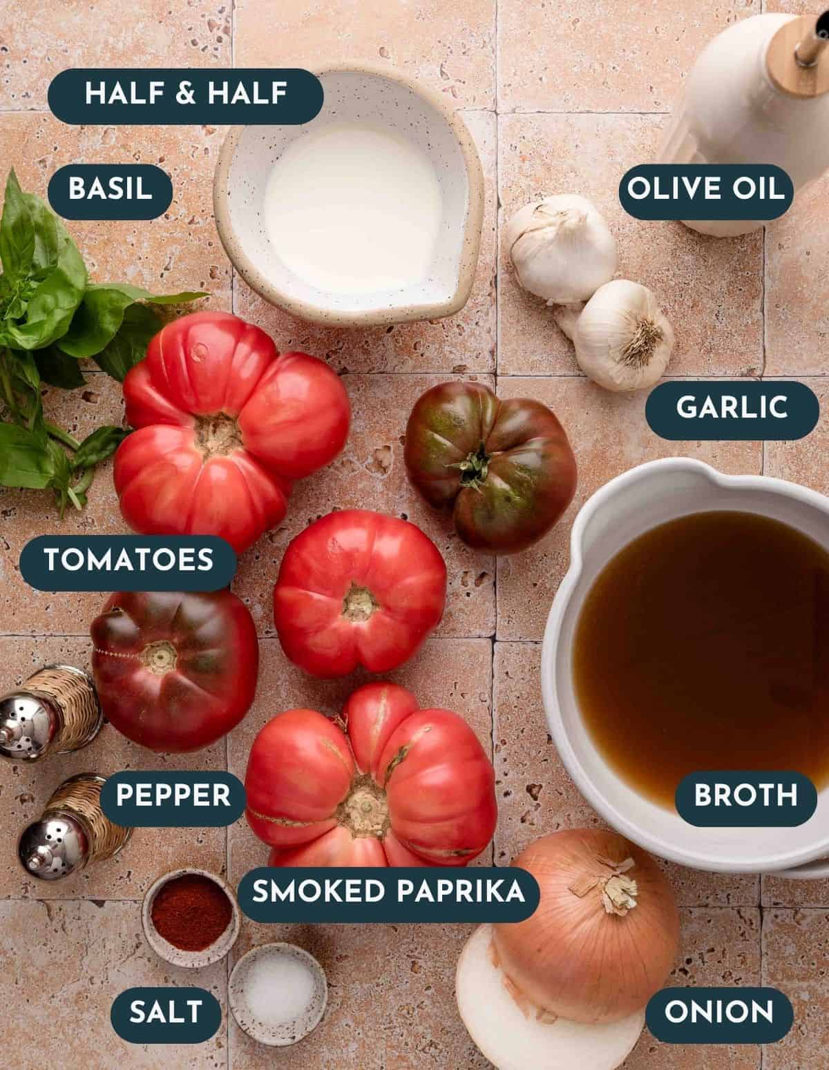Fresh tomatoes, basil, broth, half & half, garlic, onion, olive oil, salt, pepper, and smoked paprika on a counter.