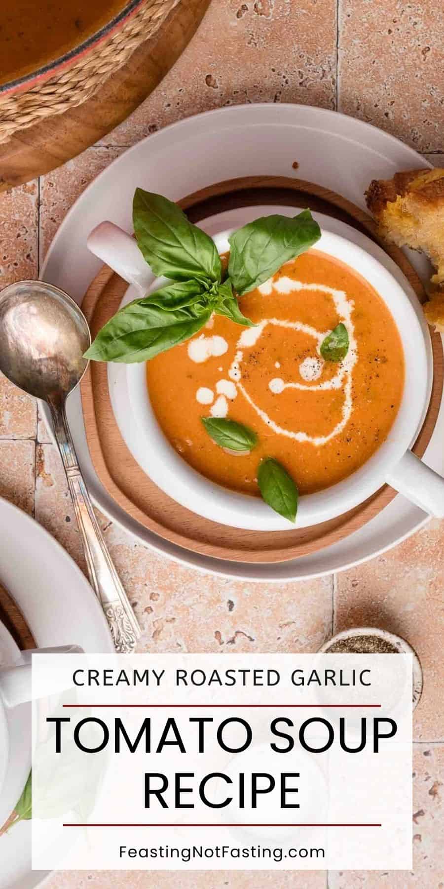 Bowl of Roasted Garlic Tomato Soup with cream and basil garnish, spoon on the side, bread and pepper nearby.